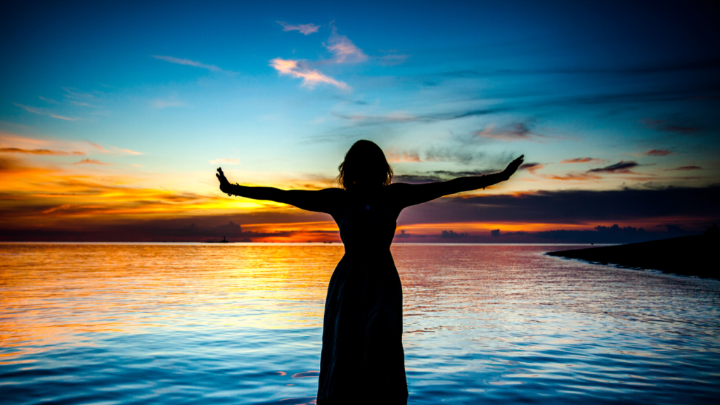 Woman by ocean with hands and heart expanded receiving transformational healing